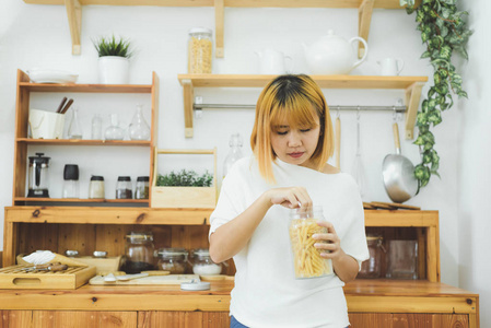 亚洲女人在家里的厨房里拿着和吃垃圾食品零食和薯片，女人喜欢不健康的食物。 生活方式妇女放松和享受垃圾食品在厨房在家里的概念。