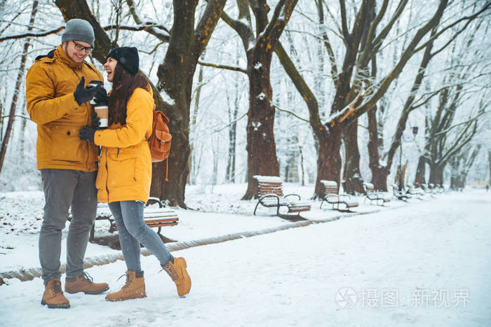 一对夫妇在下雪的城市公园边散步，谈论社交。 冬天的浪漫约会。 圣诞节快到了