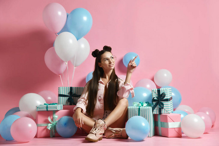 一个可爱的打扮的年轻女人坐在地板上的气球和礼品盒。 生日概念单身派对婚礼