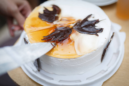 一个女人开始用刀切一个圆的白色蛋糕，上面装饰着各种形状的巧克力