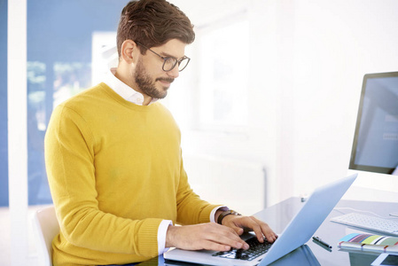 年轻商人的肖像使用他的笔记本电脑和打字时，坐在办公室和工作。