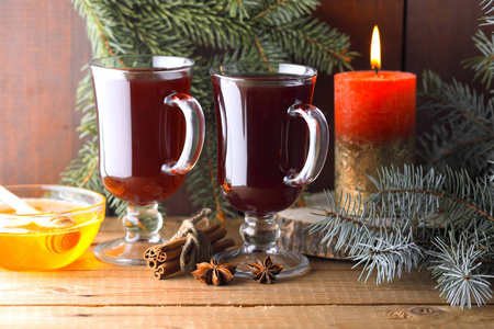 在木板上覆盖葡萄酒和燃烧蜡烛。 圣诞覆盖葡萄酒，肉桂棒，八角和蜂蜜。 酒水果和蜂蜜的酒精饮料。 节日饮料和圣诞树树枝