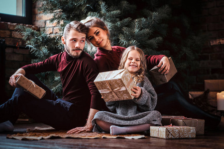 有吸引力的家庭坐在圣诞树旁边的地板上打开礼物