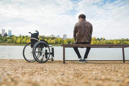 一个年轻人坐在湖边的长凳上, 旁边是他的轮椅