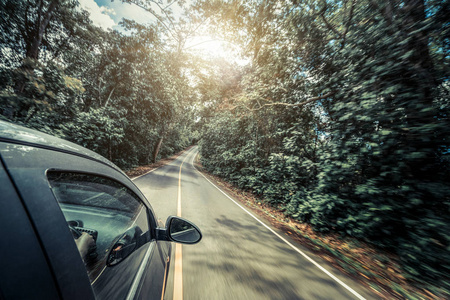 夏季在森林公路上行驶的黑色汽车的侧视图。 旅行和探索概念。
