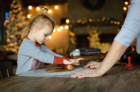 奶奶帮助她的孙女推出面团，为传统的圣诞姜饼。 一起在装饰有圣诞树和花环的房子里做饭。 家庭友好的圣诞节概念。