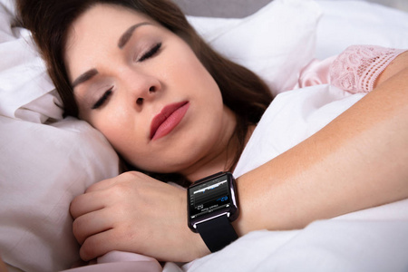 美丽的女人睡在床上智能手表显示心跳率