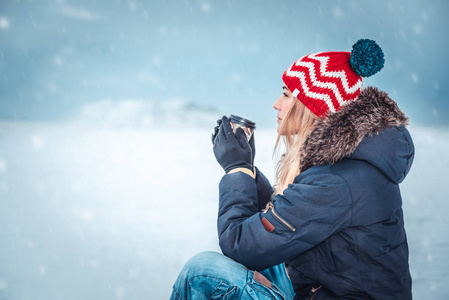 一个漂亮的女孩坐在外面的雪天，喝着咖啡，享受着宁静的寒假