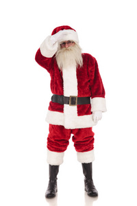 快乐的圣尼克穿着圣诞老人的服装站在白色的背景上，手牵着额头，远远地看着全长的照片