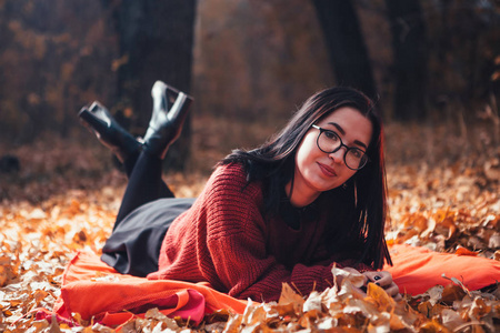 女孩躺在格子布上，在秋天的森林自然背景下。