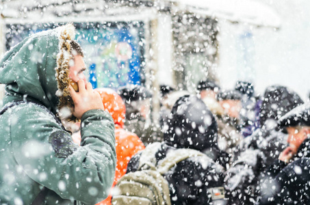 在暴风雪中，引擎盖里的人在打电话。 城市环境中的暴风雪。 降雪时公共汽车站的人。 冬季天气背景