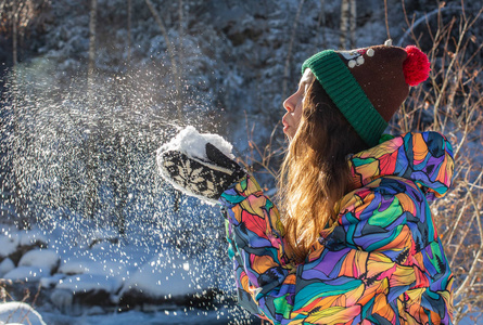 美丽的冬天女孩吹雪在寒冷的冬季公园.户外.飞行雪花.晴天.背光.