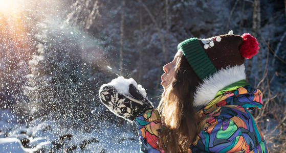 美丽的冬天女孩吹雪在寒冷的冬季公园.户外.飞行雪花.晴天.背光.