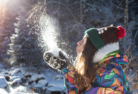 美丽的冬天女孩吹雪在寒冷的冬季公园。户外。飞行雪花。晴天。背光。快乐的美女年轻女子在冬季公园玩耍