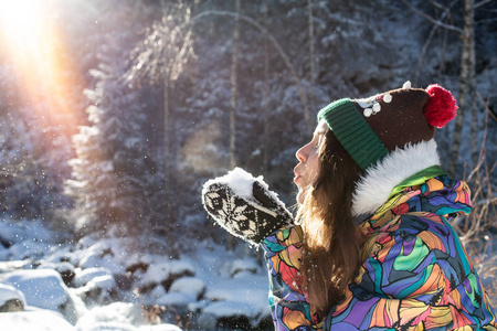 美丽的冬天女孩吹雪在寒冷的冬季公园。户外。飞行雪花。晴天。背光。快乐的美女年轻女子在冬季公园玩耍