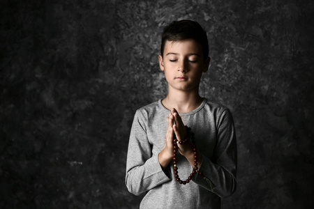 在黑暗背景下祈祷的小男孩