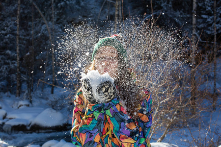 美丽的冬天女孩吹雪在寒冷的冬季公园。户外。飞行雪花。晴天。背光。快乐的美女年轻女子在冬季公园玩耍