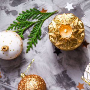 灰色背景上的圣诞装饰品，闪闪发光的星星和绿色的圣诞树树枝之间有金色的蜡烛。 顶部视图
