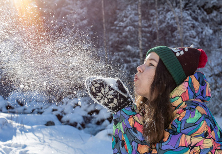 美丽的冬天女孩吹雪在寒冷的冬季公园。户外。飞行雪花。晴天。背光。快乐的美女年轻女子在冬季公园玩耍