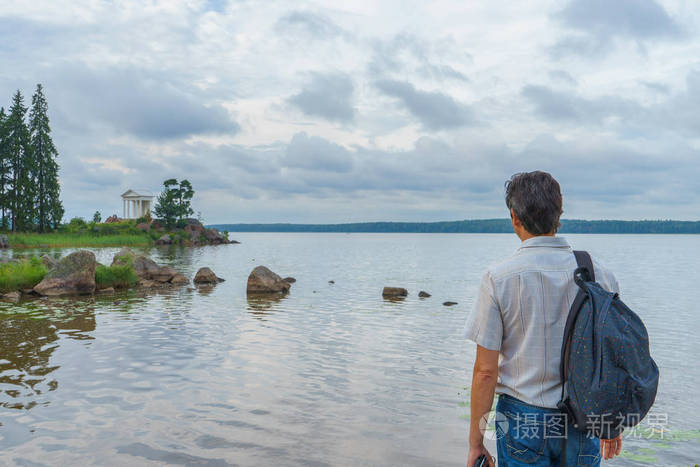 夏天晚上,英俊的中年男子背着背包站在海湾岸边.