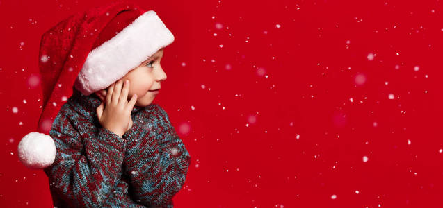 三岁的小男孩戴着圣诞老人的帽子坐在地板上。 等待礼物和假期的概念。
