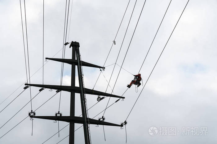 在高压电线上工作的专业人员在格子交叉上做危险的电气工作