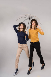 两个漂亮女孩在灰色背景下相互隔离的伞下微笑着走在一起的完整图像