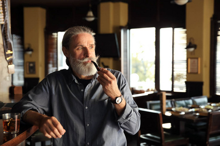 酒吧里拿着威士忌和烟斗的老人照片