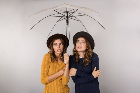 两个戴着帽子的女孩站在灰色背景下的伞下