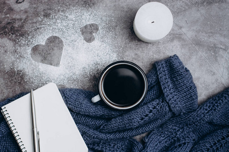 灰色桌子上有一杯咖啡蜡烛笔记本钢笔和温暖的羊毛衫。冬季概念。平躺，俯视。情人节。