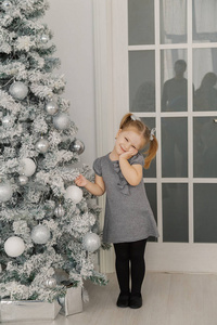 一个小女孩站在圣诞树旁触摸玩具