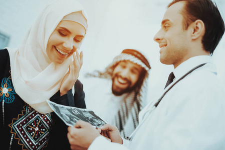 快乐怀孕的穆斯林妇女持有超声波图像。 医生拿着超声波图像。 怀孕的女人。 妇科医生的概念。 做母亲。 阿拉伯女人戴着头巾在医院里