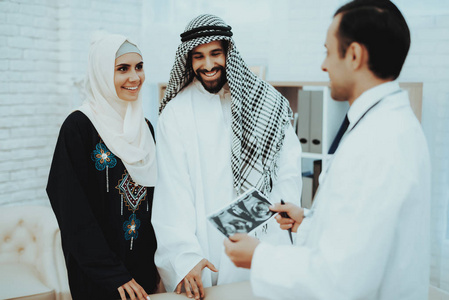 快乐怀孕的穆斯林女人和阿拉伯语的丈夫。 医生拿着超声波图像。 怀孕的女人。 妇科医生的概念。 做母亲。 阿拉伯女人戴着头巾在医院