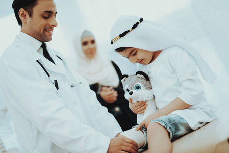 儿童患者阿拉伯男性医生包扎肢体。 医院概念。 健康的概念。 儿童病人出诊医生。 医生包扎腿小天井。 儿童病人出诊医生。 腿伤