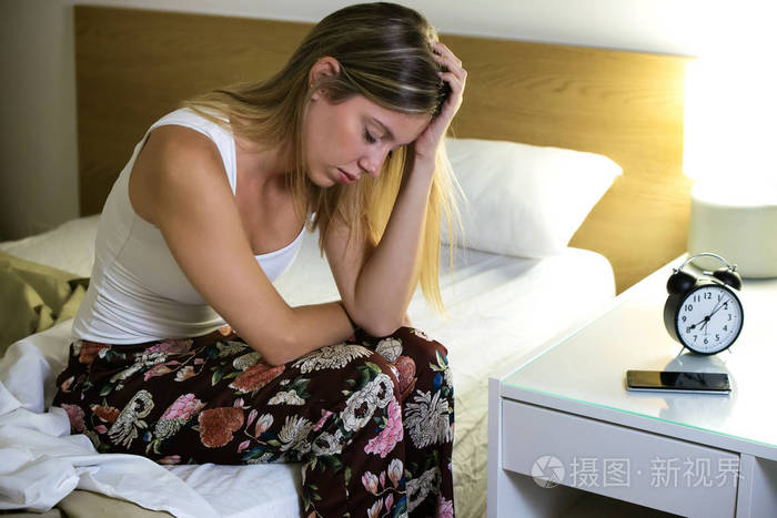 一个美丽的年轻疲惫的女人在家里的卧室里坐在床上失眠.