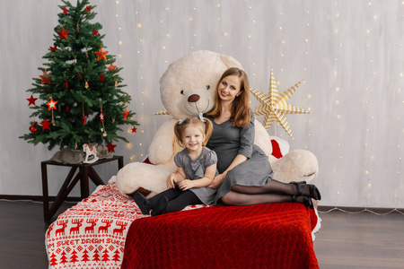 非常漂亮的女孩和她的孩子在床上与熊在圣诞房间