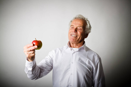 穿白衣服的老人拿着一个苹果。