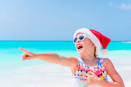 快乐有趣的小女孩在圣诞老人的帽子在圣诞节海滩假期有很多的乐趣