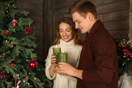 爱的年轻夫妇在家附近的圣诞树旁点燃蜡烛
