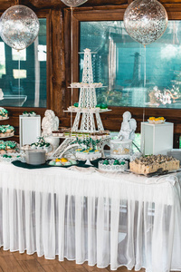 绿色风格的婚礼糖果棒上的白色桌子。用绿色丝带蝴蝶结装饰的纸杯蛋糕