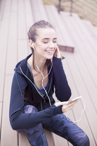 运动型年轻女子在城市环境户外训练后，在手机上休息和听音乐
