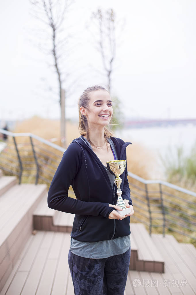 成功的年轻女子在户外捧起奖杯
