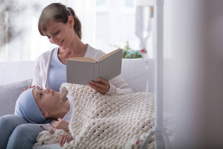带着头巾的生病的孩子带着微笑的母亲读书