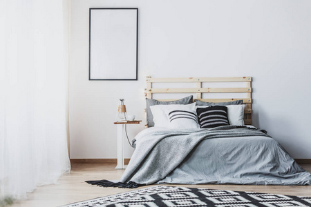 白色卧室内的空海报模型，灰色带靠垫的木床。真照片