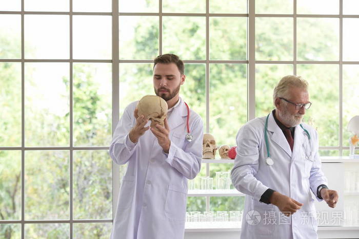 这位老医生向年轻医生解释了生理知识。医生在医院一起工作和使用头骨和塑料脑模型