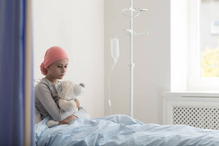 患有癌症的悲伤孩子在医院里拥抱毛绒玩具，滴水