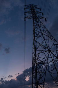 高压电力传输塔形轮廓与发电厂对暗灯天空。