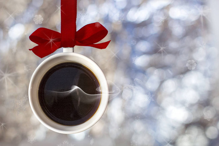 圣诞卡杯香的热咖啡与烟雾制成的圣诞球宝布尔挂在红色丝带的背景上，离焦的银灯。 新年的概念节日标志