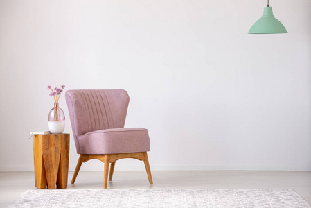 木制凳子上的花，旁边的粉红色扶手椅在平坦的内部与复制空间和薄荷灯。 真实照片