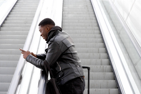 乘手机和电扶梯旅行的酷青年黑人肖像